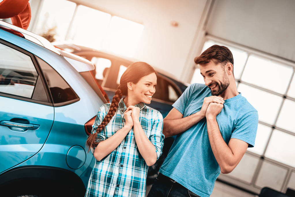 Young Family Are Choosing A New Car In Showroom. Staring At Each Other. Automobile Salon. Make A Decision. Gift Ribbon. End Of A Deal. Good Offer. Happy Together. Successful Buying. - Photo, Image