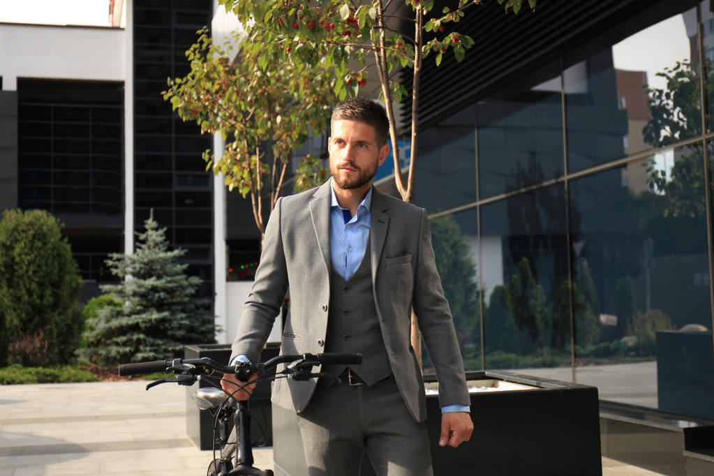 Уверенный молодой бизнесмен, гуляющий на велосипеде по улице в городе
. - Фото, изображение
