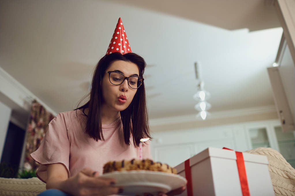 Una chica en una gorra sola con un pastel con velas en la habitación
. - Foto, Imagen