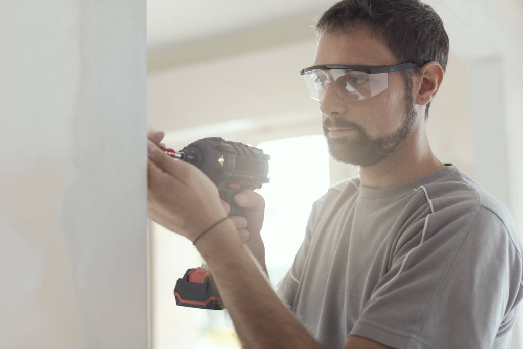 Professional repairman with protective goggles, he is using a drill and doing a home renovation - Photo, Image