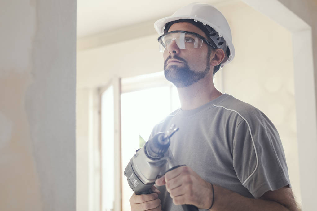 Bir matkap kullanarak profesyonel inşaat işçisi bir kask giyiyor ve koruyucu gözlük - Fotoğraf, Görsel