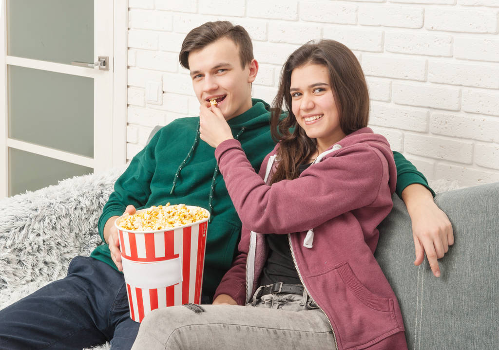 Два подростка сидят на диване и смотрят телевизор.
 - Фото, изображение