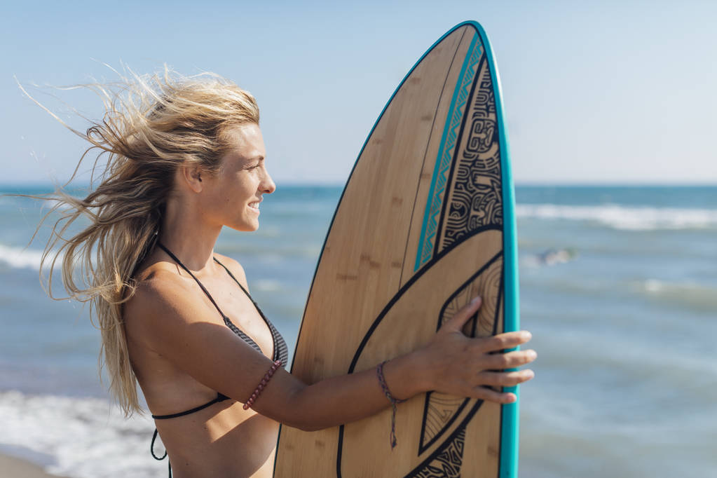 Портрет красивої блондинки-серфера, що стоїть на пляжі
. - Фото, зображення