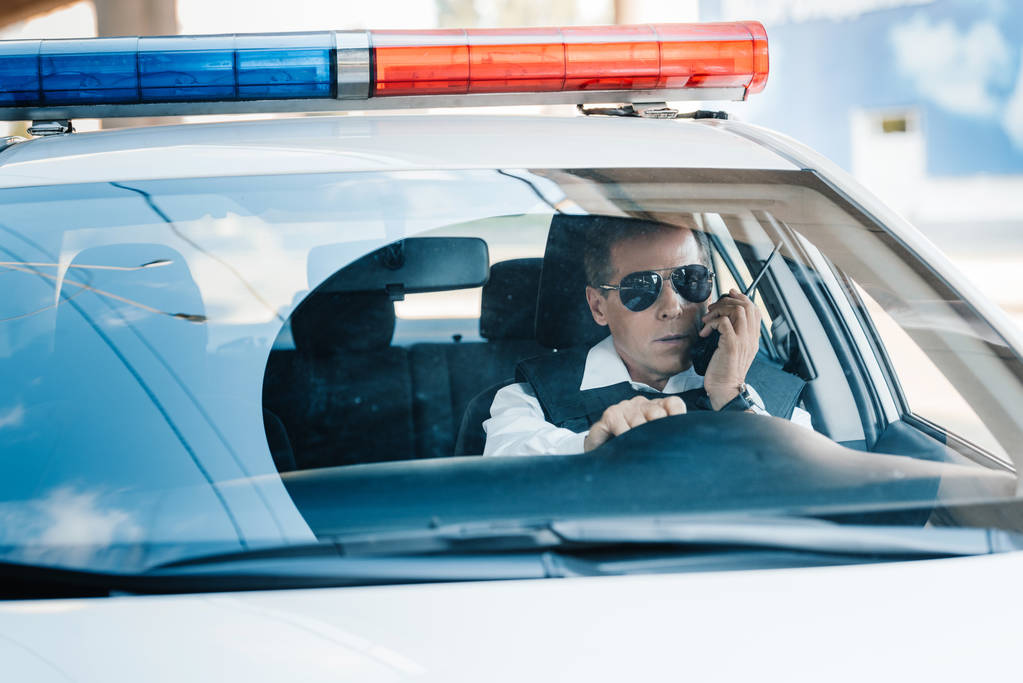 σοβαρή μέσης ηλικίας αστυνομικός σε γυαλιά ηλίου, μιλώντας στο ραδιόφωνο στο αυτοκίνητο  - Φωτογραφία, εικόνα