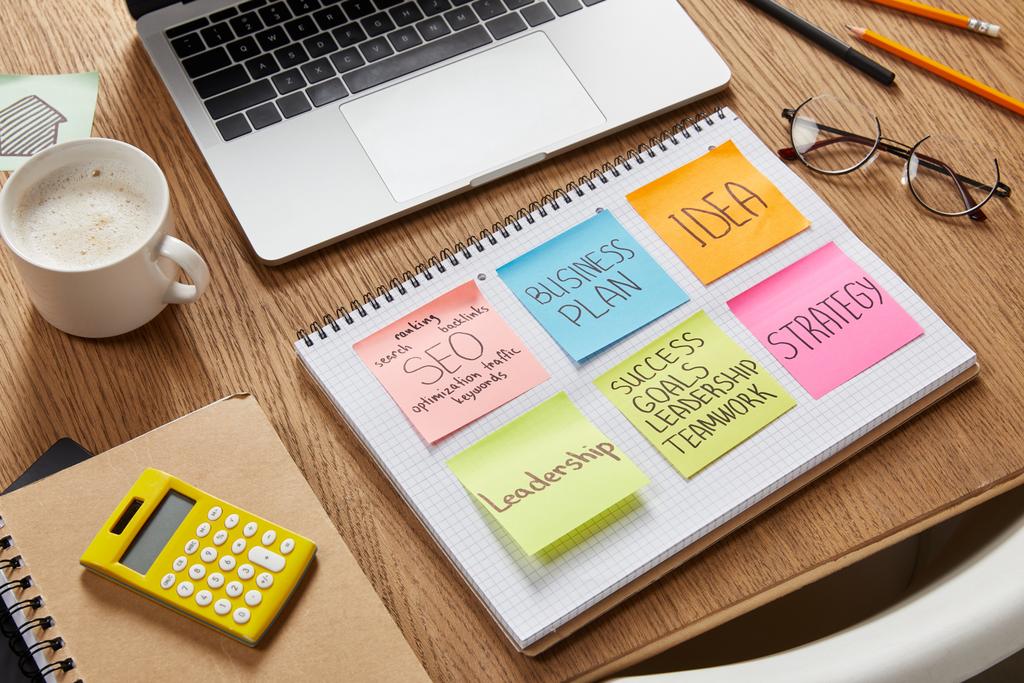 adesivos de papel com estratégia de negócios, calculadora, xícara de café e laptop na mesa
 - Foto, Imagem