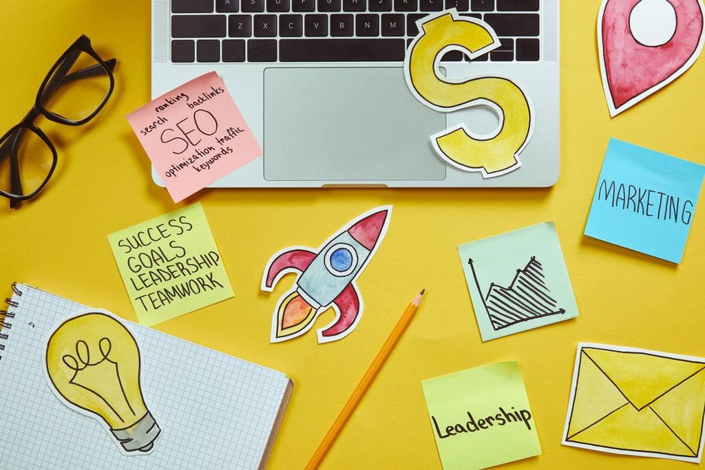 top view of laptop, paper signs and paper stickers with business plan on yellow surface - Photo, Image