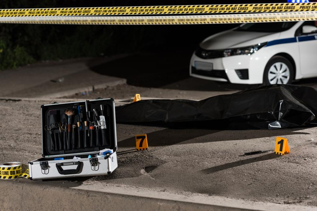 caso com ferramentas de investigação, carro, linha de polícia e cadáver em saco de corpo na cena do crime
  - Foto, Imagem
