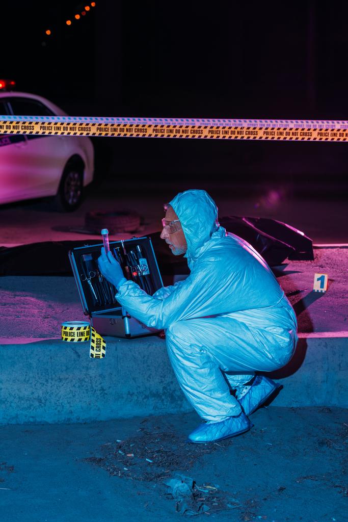 Μερική άποψη του επικεντρωμένη αρσενικό Εγκληματολόγος προστατευτικά ενδύματα και γάντια από λάτεξ συλλογής αποδεικτικών στοιχείων στη σκηνή του εγκλήματος με πτώμα  - Φωτογραφία, εικόνα