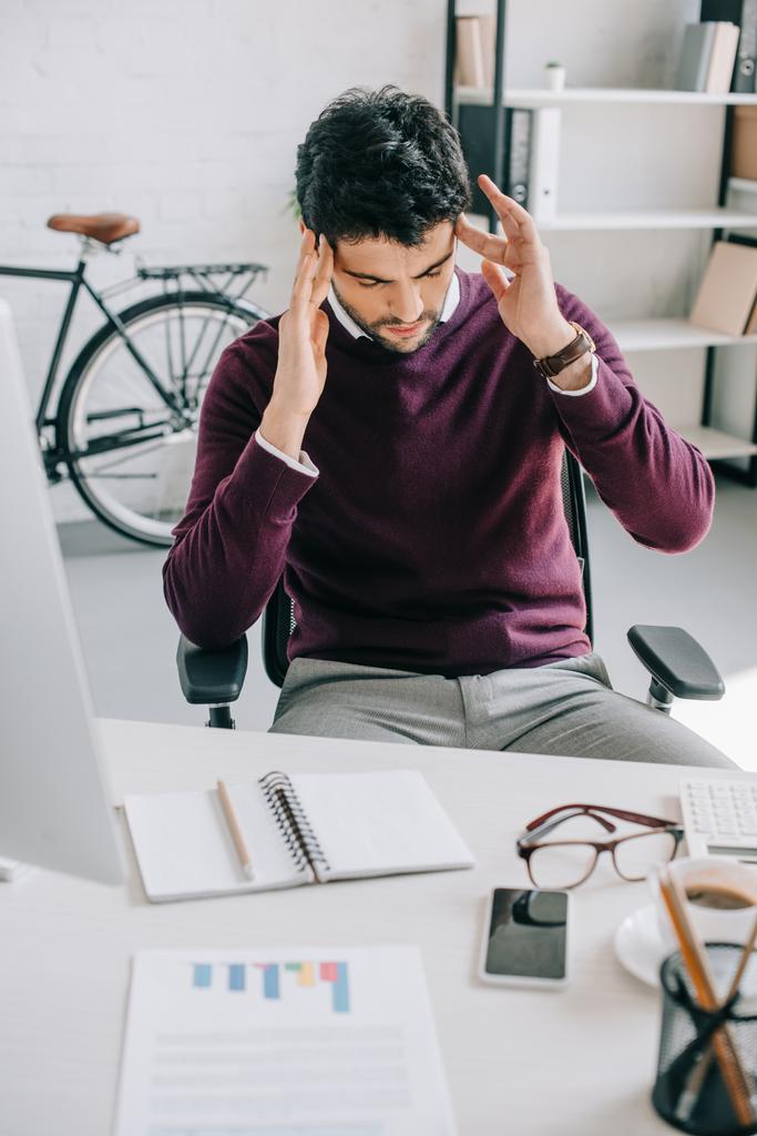 усталый дизайнер в бордовом свитере с головной болью в офисе
  - Фото, изображение