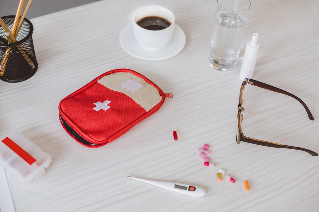 botiquín de primeros auxilios, taza de café y pastillas en la mesa en la oficina
 - Foto, Imagen