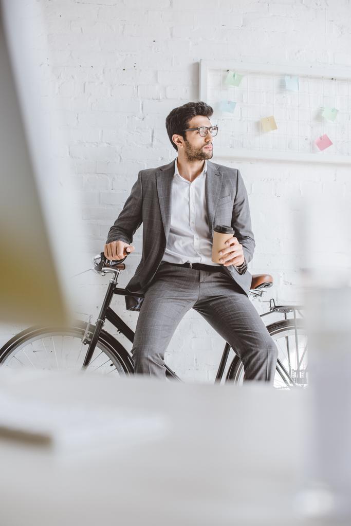 красивый бизнесмен сидит на велосипеде и держит кофе, чтобы пойти в офис
 - Фото, изображение