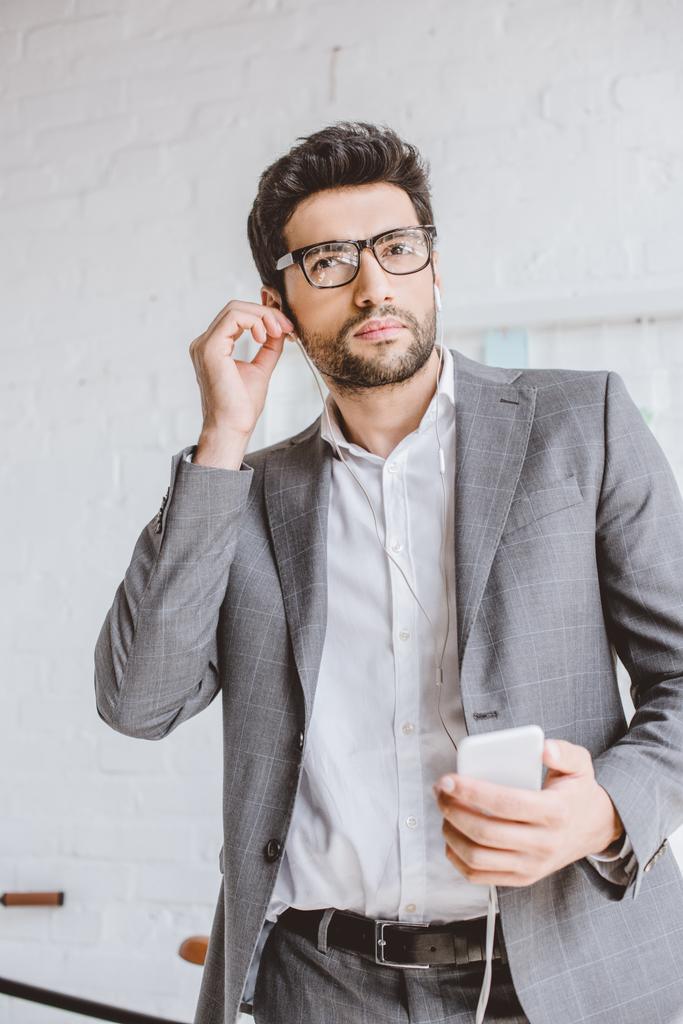 homem de negócios bonito conectando fones de ouvido para ouvir música no escritório
 - Foto, Imagem