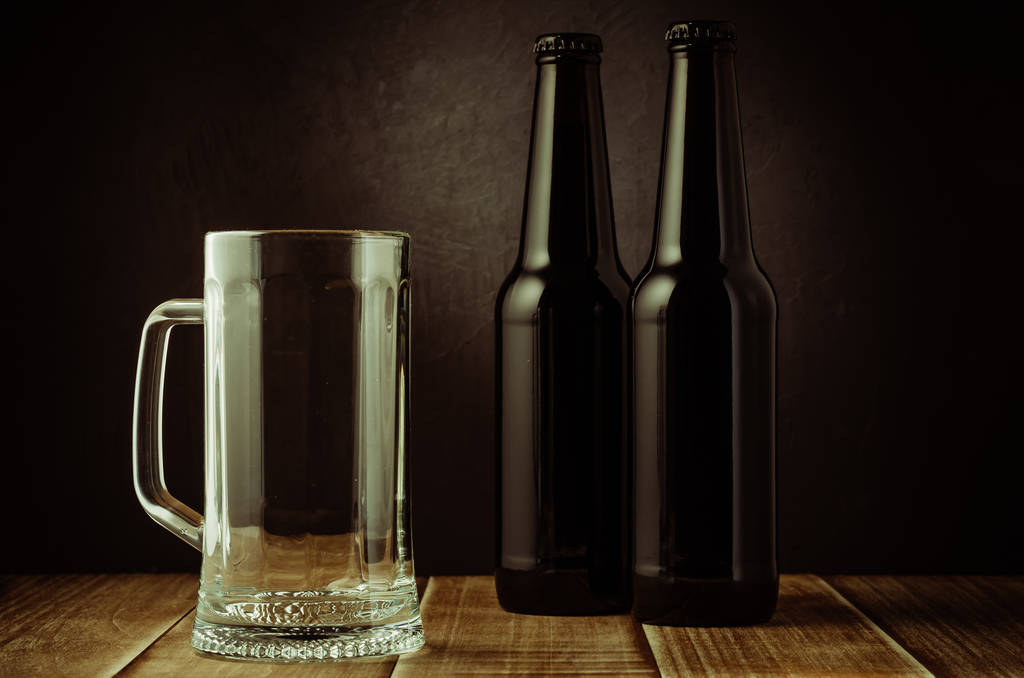 taza de cerveza vacía y botella sobre un fondo oscuro / taza de cerveza vacía y botella sobre un fondo oscuro. Enfoque selectivo
 - Foto, Imagen