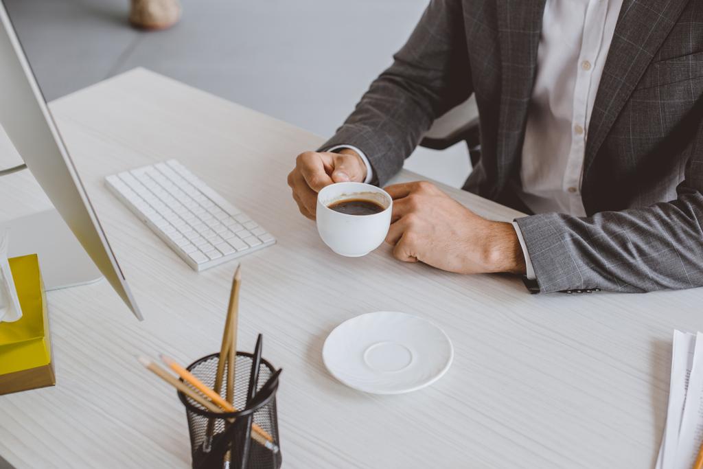 обрізане зображення бізнесмена, що тримає чашку кави за столом в офісі
 - Фото, зображення