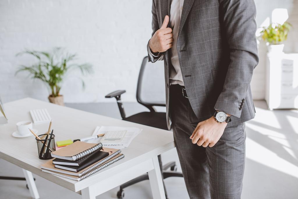 imagen recortada de hombre de negocios de pie en traje gris y con reloj de pulsera en la oficina
 - Foto, imagen