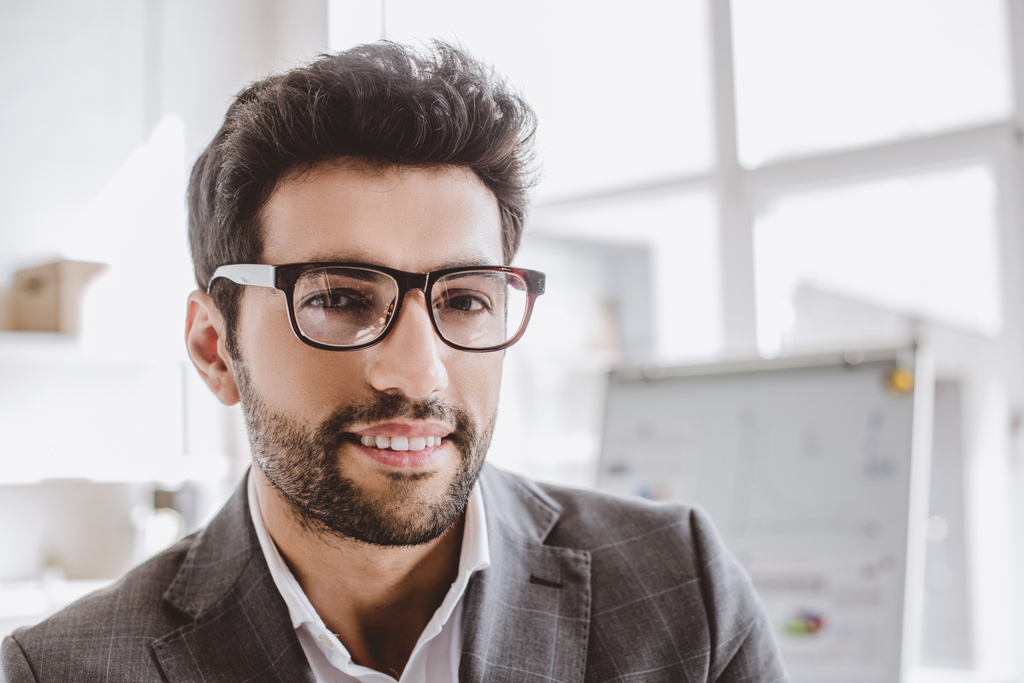 portrait of smiling handsome businessman in glasses looking at camera in office - Photo, Image