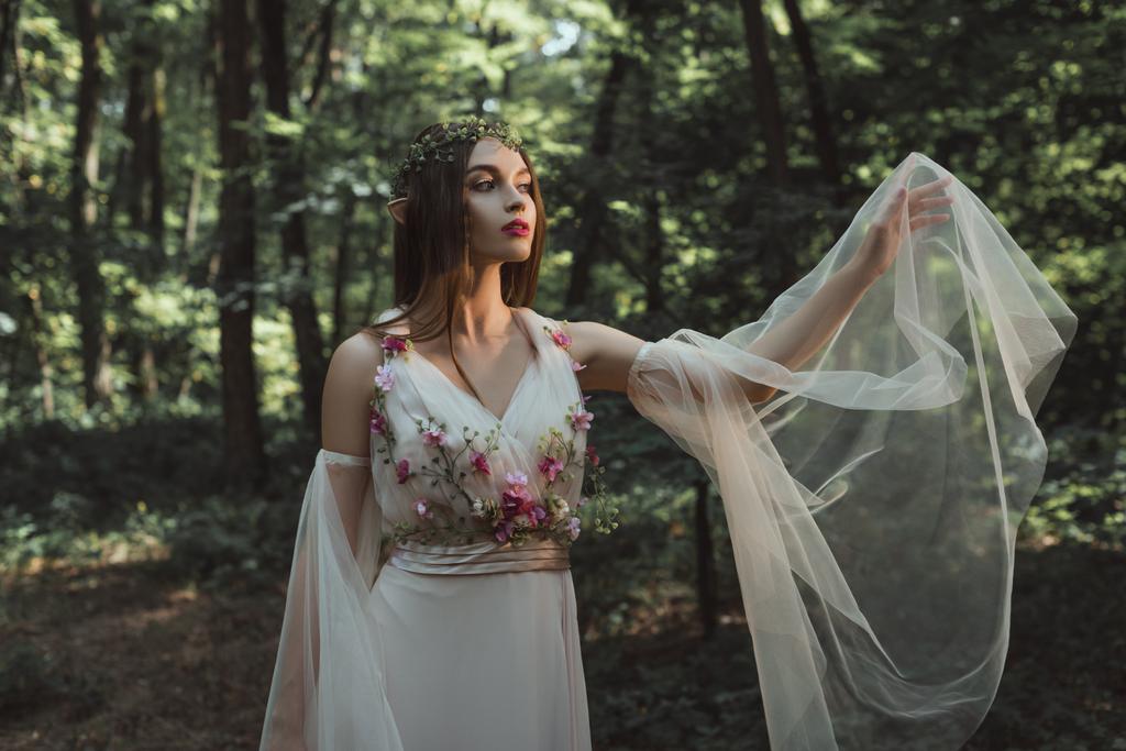 mystic elf in elegant dress with flowers in forest - Photo, Image