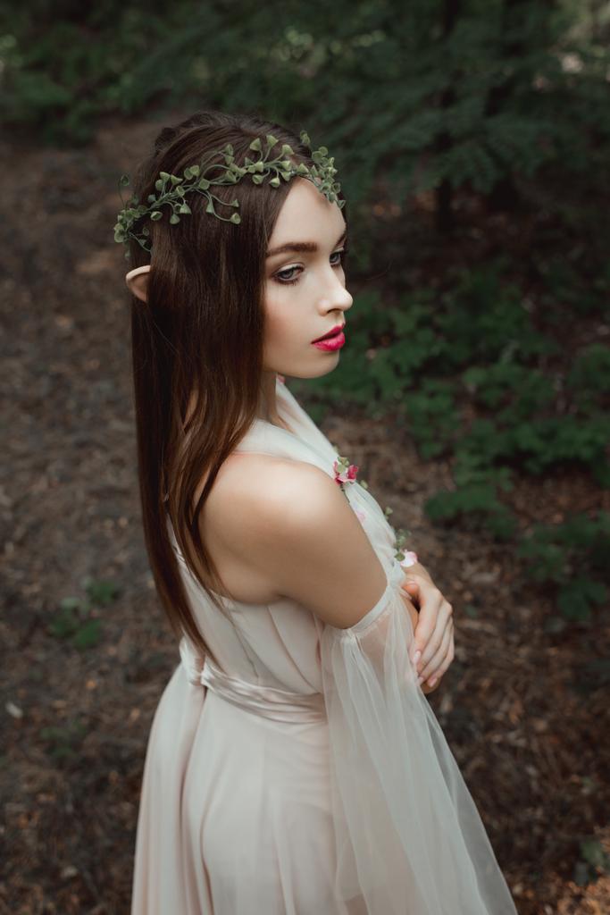 mystic elf in elegant dress and floral wreath in forest - Photo, Image