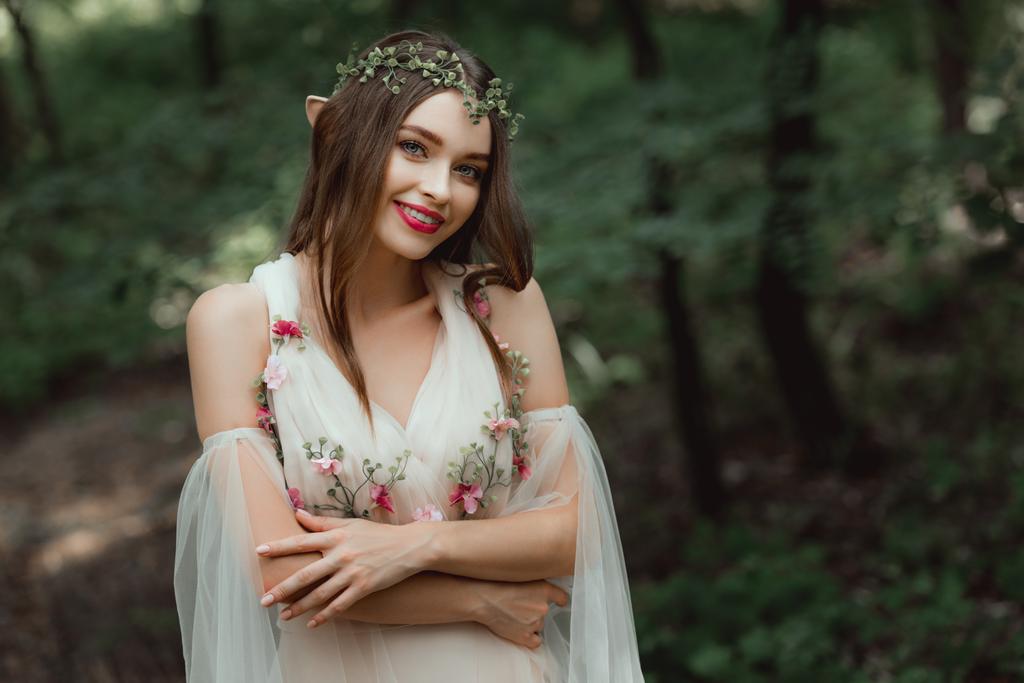 çekici gülümseyen kız elbise ve çiçek çelenk ormanda poz - Fotoğraf, Görsel