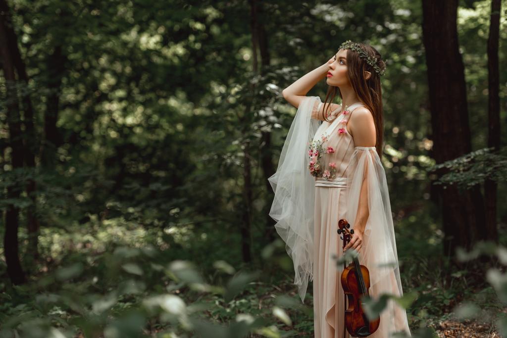 mystic elf character in flower dress holding violin in green forest - Photo, Image
