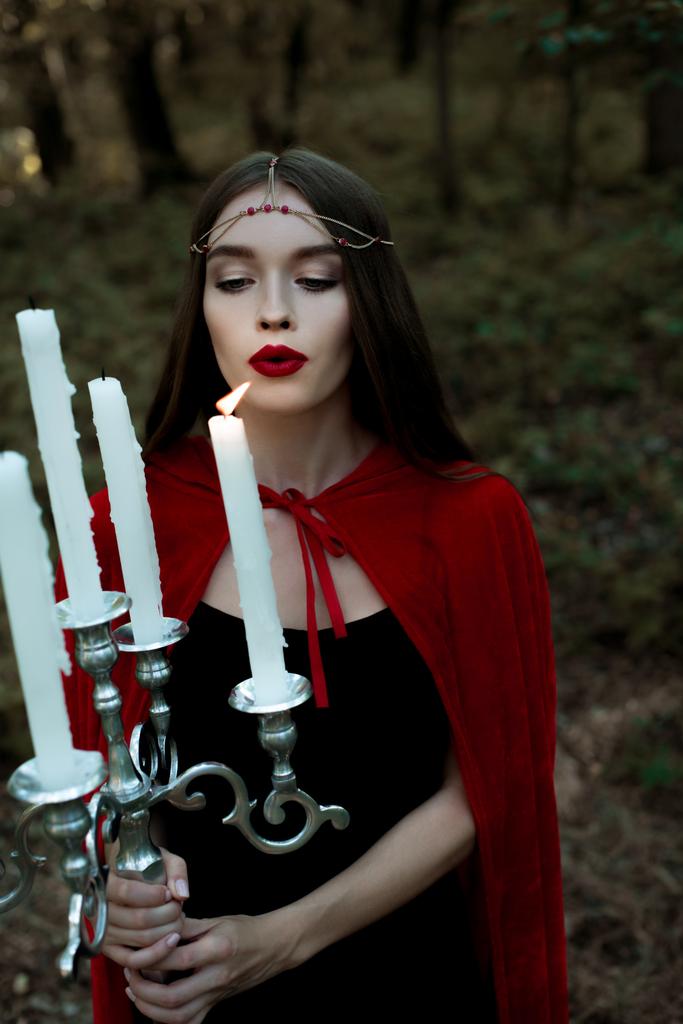 bela menina mística em manto vermelho e grinalda soprando velas
  - Foto, Imagem