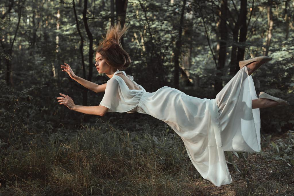 tyylikäs nuori tarjouksen nainen valkoinen mekko lentää metsässä
 - Valokuva, kuva