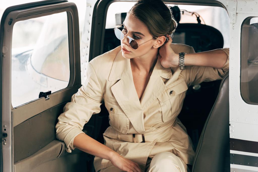 молодая стильная женщина в солнцезащитных очках и куртке позирует в самолете
  - Фото, изображение