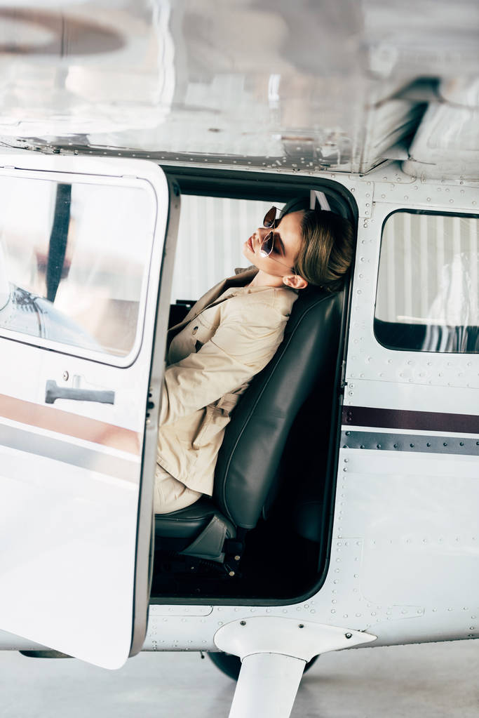 side view of stylish woman in sunglasses and jacket sitting in airplane  - Photo, Image