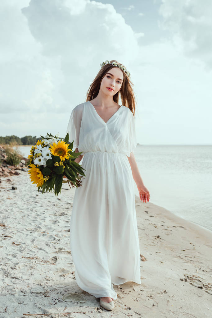 κομψό κορίτσι σε λευκό φόρεμα κρατώντας την ανθοδέσμη και το περπάτημα στην παραλία - Φωτογραφία, εικόνα