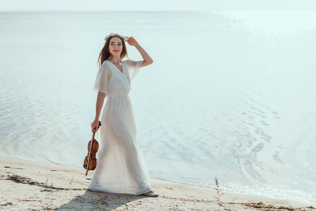 όμορφη γυναίκα στο κομψό φόρεμα με βιολί, περπάτημα στην παραλία κοντά στη θάλασσα - Φωτογραφία, εικόνα