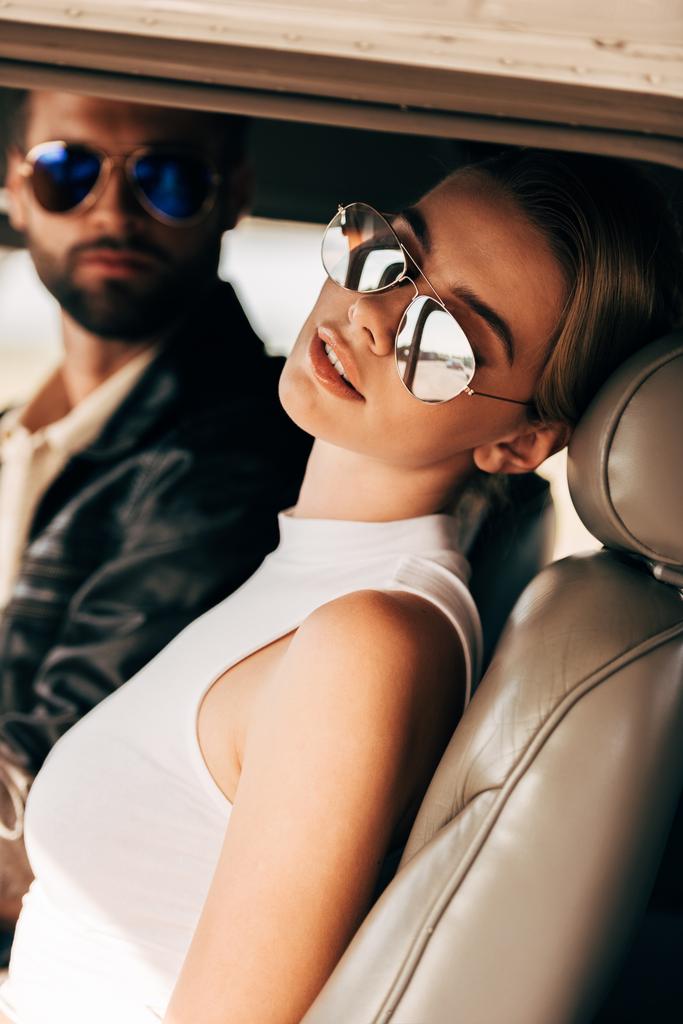 foco seletivo da bela jovem mulher em óculos de sol sentado perto do piloto masculino na cabine do avião
  - Foto, Imagem