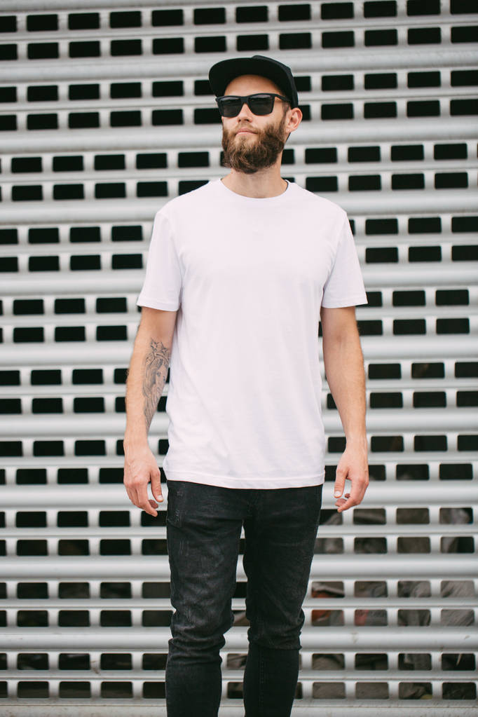 Hipster knappe mannelijke model met baard dragen witte lege t-shirt en een baseballcap met ruimte voor uw logo - Foto, afbeelding