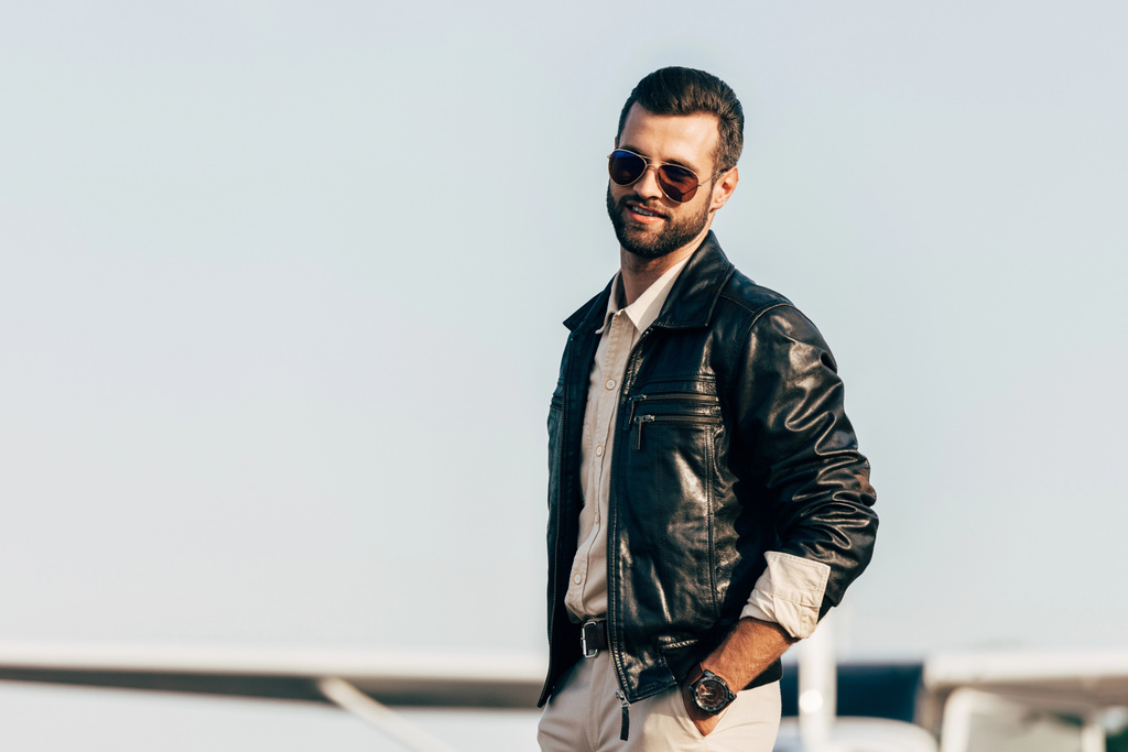 jeune beau pilote masculin en veste en cuir et lunettes de soleil posant près de l'avion
  - Photo, image