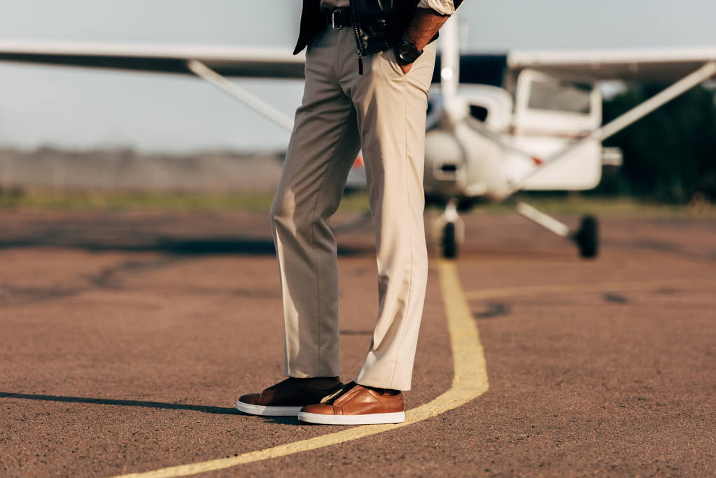 abgeschnittenes Bild eines stilvollen Mannes in Hose und Turnschuhen in Flugzeugnähe  - Foto, Bild