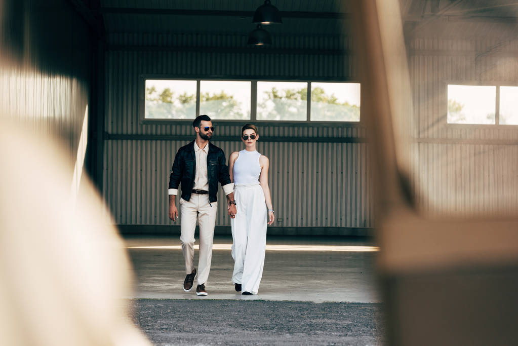 selective focus of stylish man in leather jacket and sunglasses holding hands with girlfriend  - Photo, Image