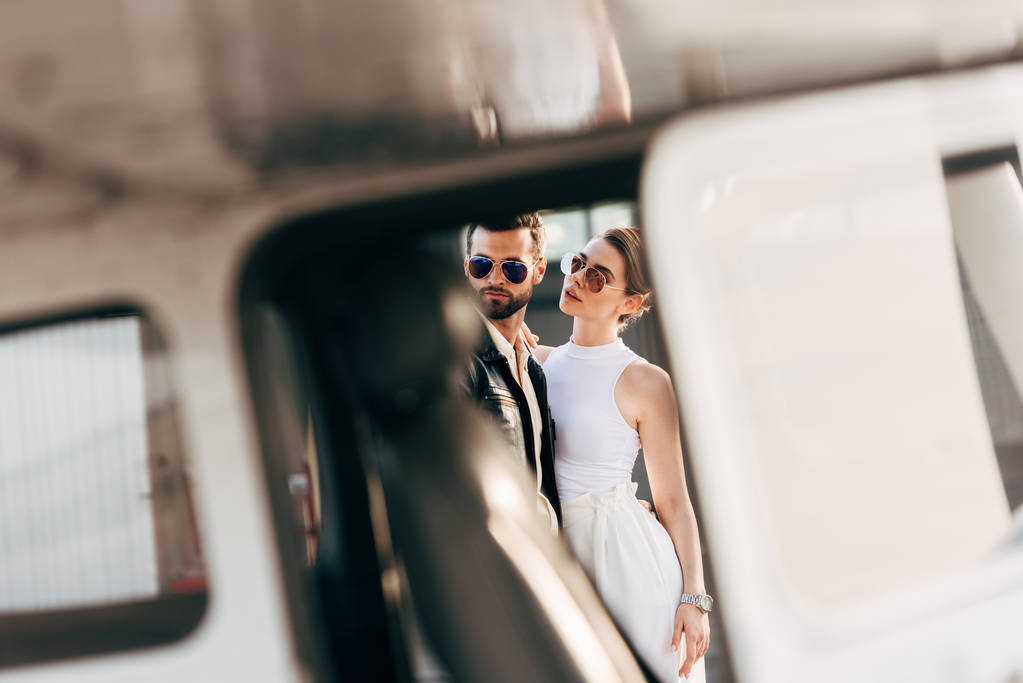 enfoque selectivo de hombre guapo en chaqueta de cuero y gafas de sol de pie con novia cerca de avión
 - Foto, Imagen
