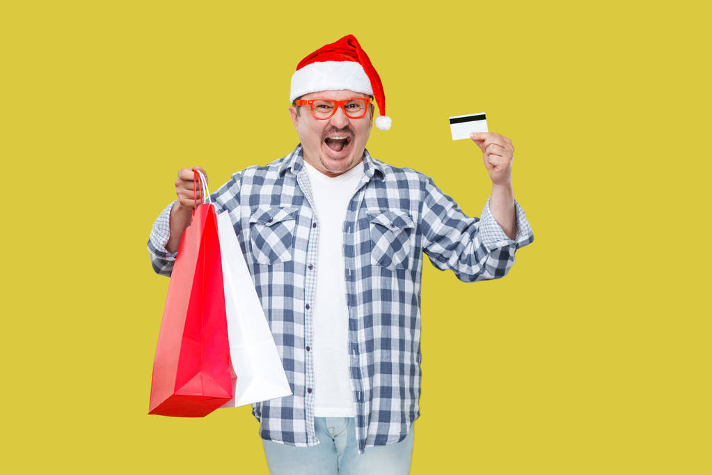 Uomo felice in cappuccio rosso che tiene borse regalo shopping e carta di credito su sfondo giallo
 - Foto, immagini