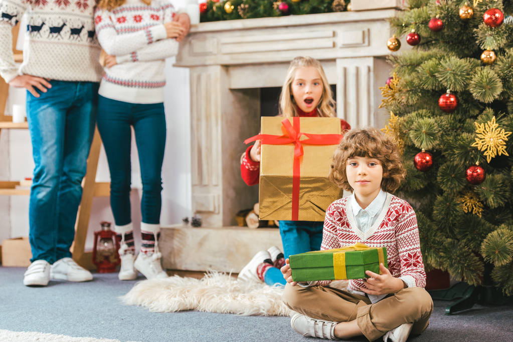 обрізаний знімок батьків, що стоять позаду дітей з різдвяними подарунками вдома
 - Фото, зображення