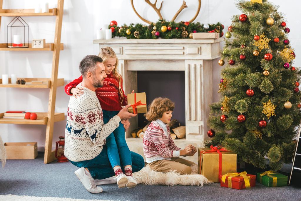 Boldog Apák és a gyerekek, figyelembe véve a karácsonyfa alatt ajándékok - Fotó, kép