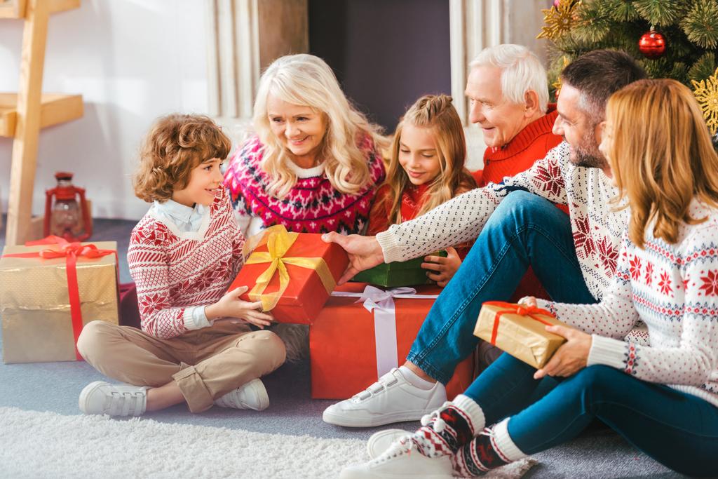 kaunis onnellinen perhe lahjapakkauksilla istuu olohuoneen lattialla joulun aikana
 - Valokuva, kuva