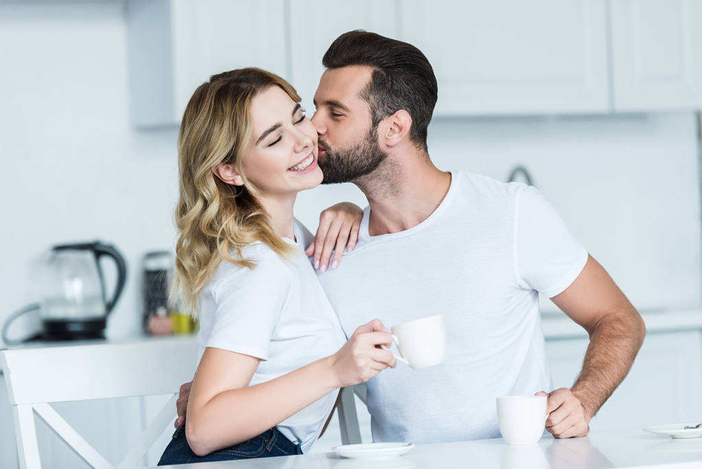 Красивый бородатый мужчина целует улыбающуюся девушку, когда пьет кофе вместе
 - Фото, изображение