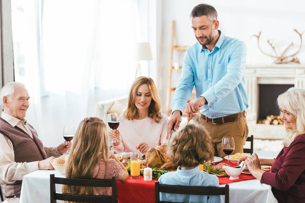 happy family having delicious thanksgiving dinner together at home while father cutting turkey - Photo, Image