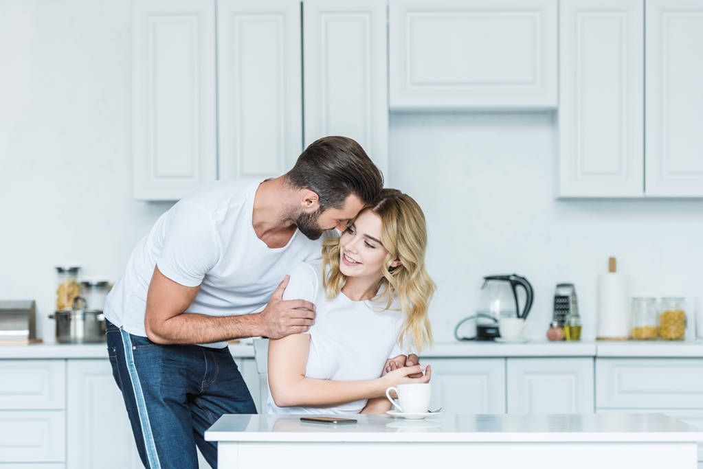 happy young couple embracing during breakfast in kitchen - Photo, Image
