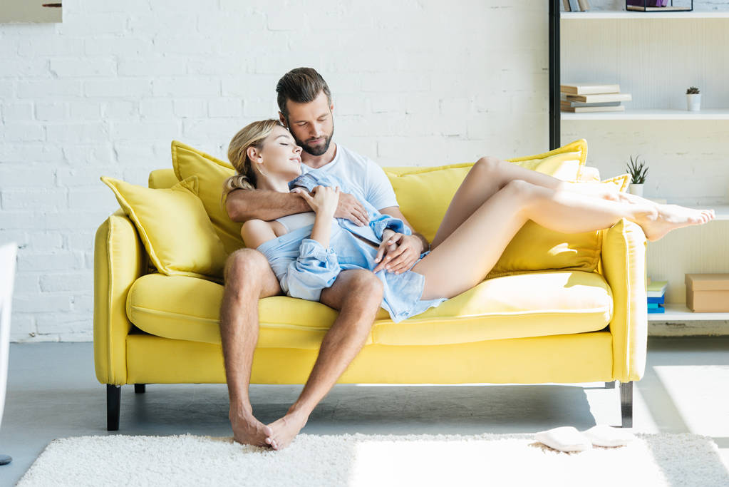bella tenera giovane coppia innamorata che si abbraccia sul divano giallo a casa
 - Foto, immagini