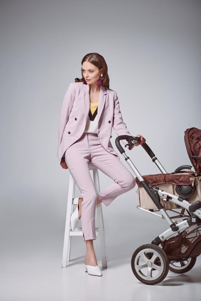 bella donna elegante con passeggino seduto sullo sgabello e guardando lontano sul grigio
 - Foto, immagini