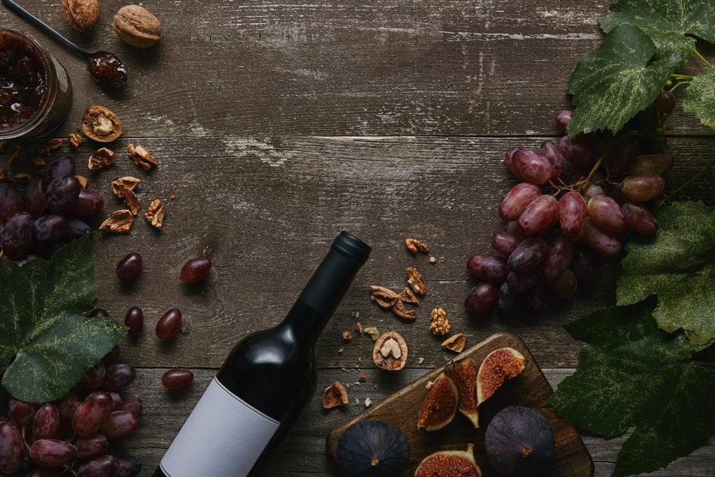 pohled shora na láhev vína s prázdný popisek, ovoce a lahodné marmelády na dřevěný stůl - Fotografie, Obrázek