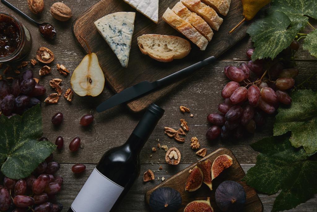 Draufsicht auf Weinflasche mit leerem Etikett, frischem Obst und leckeren Snacks auf Holztisch - Foto, Bild