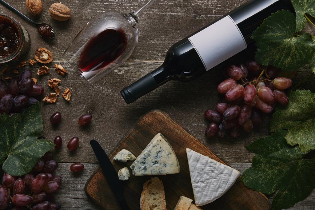 верхний вид бутылки и бокала красного вина, вкусный сыр и виноград на деревянный стол
 - Фото, изображение