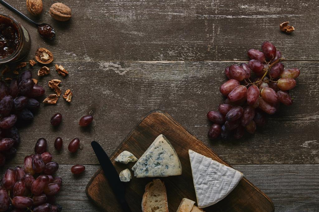 木製のテーブルに新鮮な熟したブドウ、クルミ、チーズ、おいしいジャムの上から見る   - 写真・画像