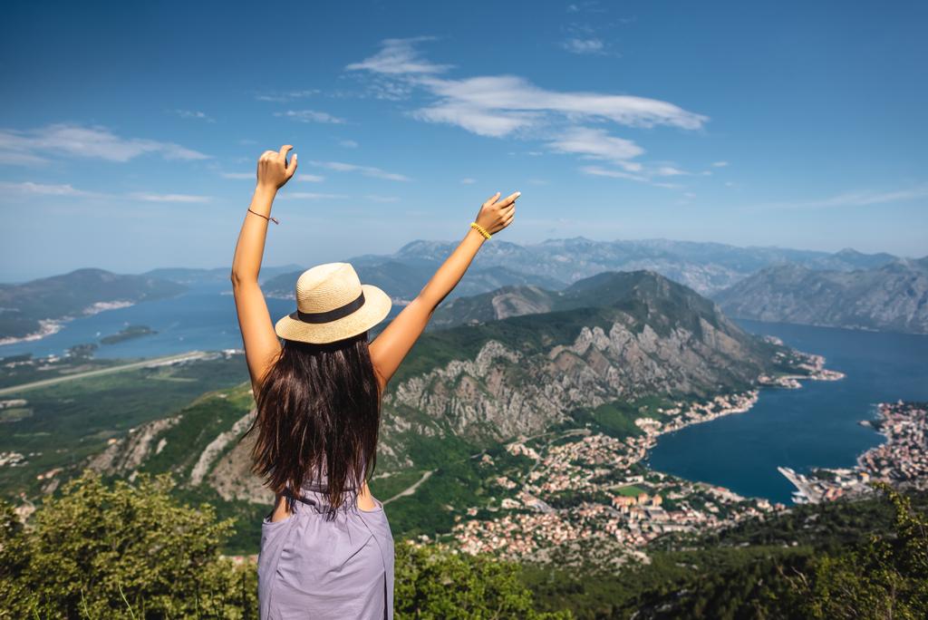 задний вид женщины, стоящей с поднятыми руками и смотрящей на Которский залив и город Котор в Черногории
 - Фото, изображение